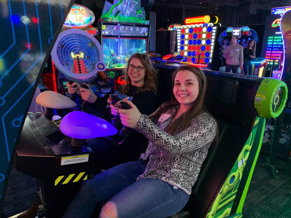 Two alumni smiling before playing arcade game